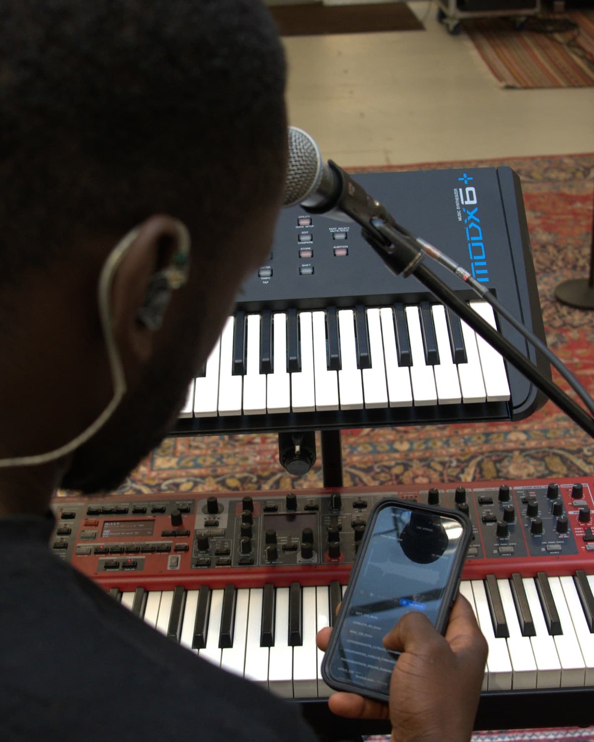 A music director at his keyboard rig during rehearsal, checking the setlist on his phone